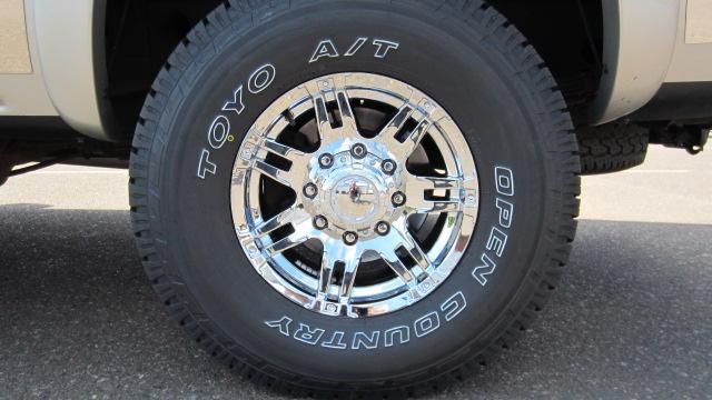 Close-up of a pickup truck tire and chrome wheel on pavement, with white lettering on the sidewall.