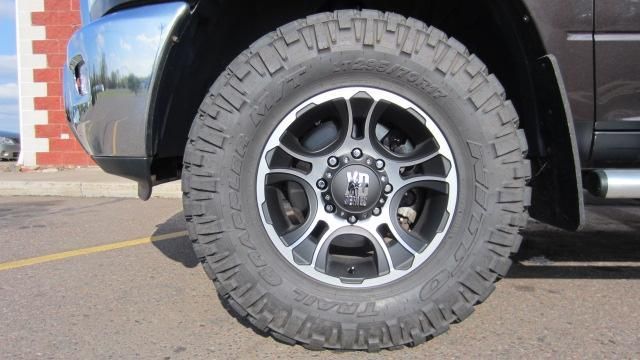 Close-up of a black truck’s off-road tire and silver wheel parked beside a brick wall.