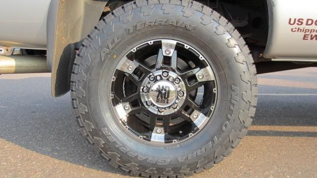 Close-up of a truck tire and black wheel parked on pavement, with part of the truck body visible.