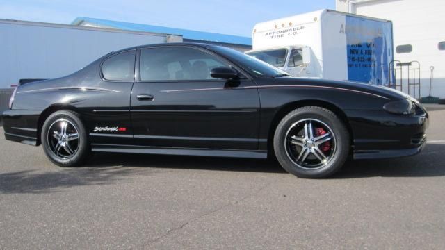 Black sports coupe parked outdoors in front of a building, side view.