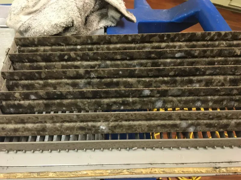 Dirty HVAC filter with dark grime and white residue, on a metal frame.