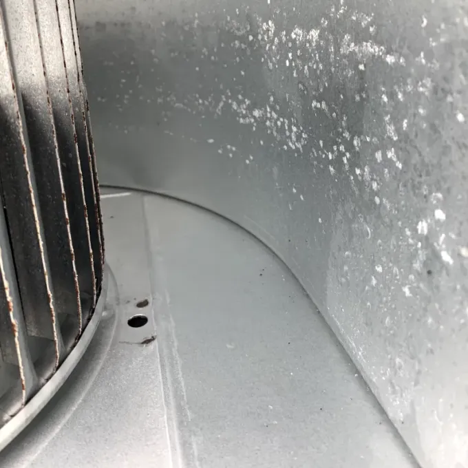 Inside of a metal blower housing, fan blades on left, white residue on the walls.