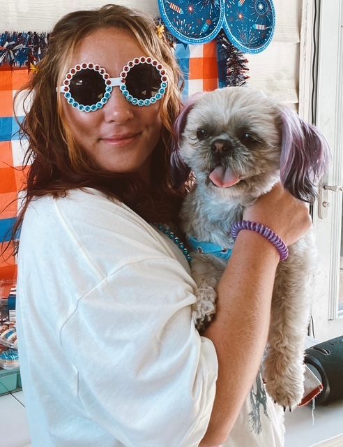 Woman in round blue sunglasses holding a small gray-and-white dog indoors. Woman in round blue sunglasses holding a small gray-and-white dog indoors.