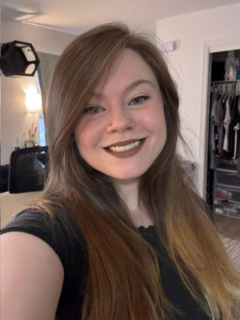 Smiling person taking a selfie in a bedroom, wearing a black shirt with long brown hair. Smiling person taking a selfie in a bedroom, wearing a black shirt with long brown hair.