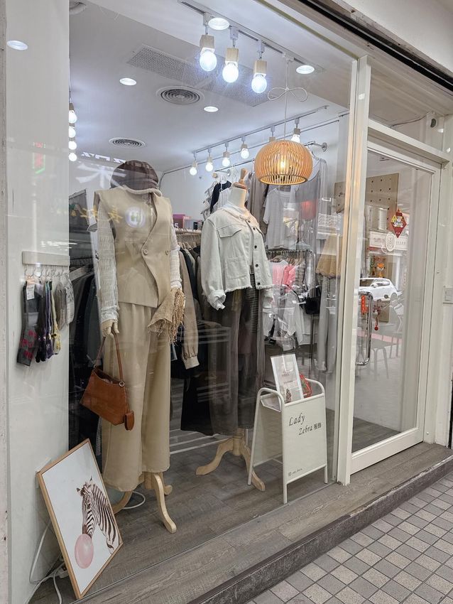 店面櫥窗展示著兩個穿著休閒服裝的人體模特，包括米色長褲和淺色牛仔外套。