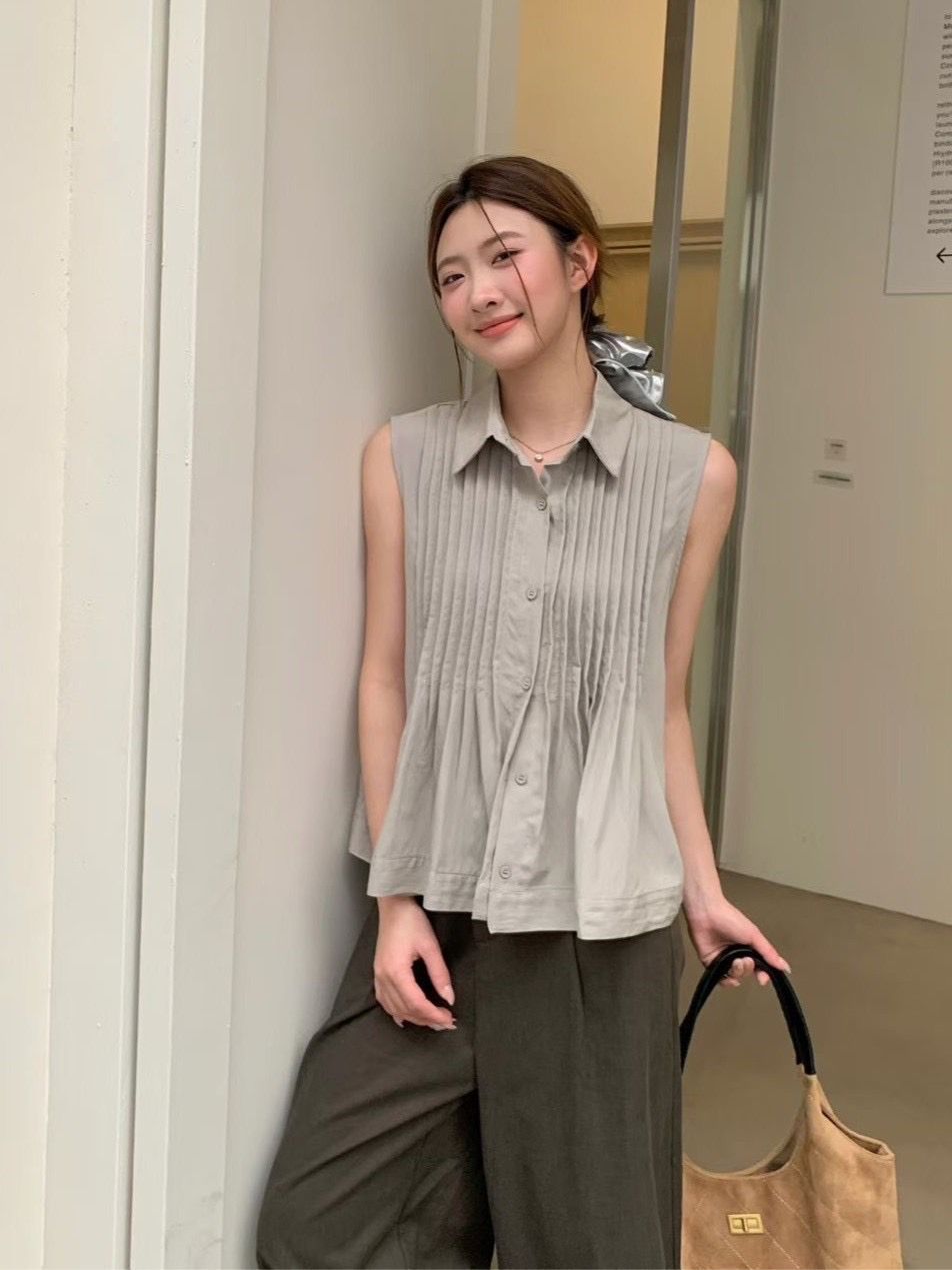 一名身穿褶皺無袖灰色羈扣襯衫和深色褲子的人倚靠在牆上，手裡拿著一個包包。