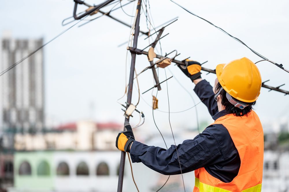An Electrician Is Working On A Power Line On Top Of A Building — Craig's TV/Antenna Services In Cardiff, NSW