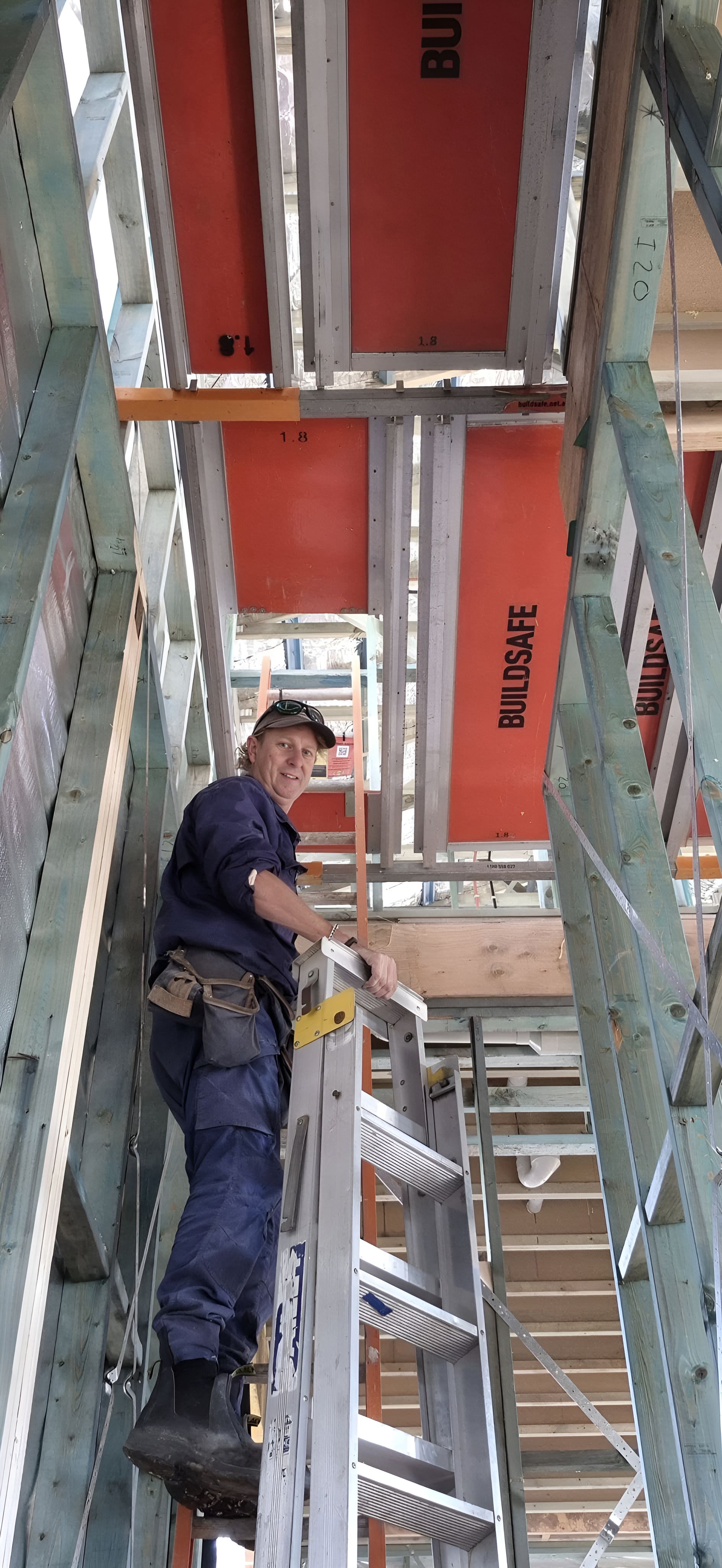A Man Is Standing On A Ladder In A Building — Craig's TV/Antenna Services In Wallsend, NSW