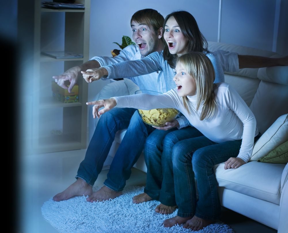 A Family Is Sitting On A Couch Watching Tv — Craig's TV/Antenna Services In Cameron Park, NSW