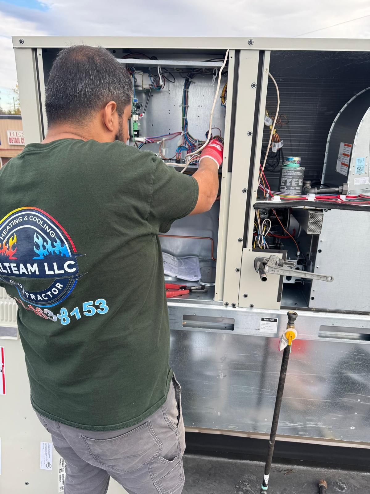 A technician in a green branded shirt works on the internal components of an outdoor commercial HVAC unit.