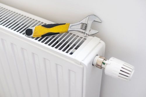 An adjustable wrench with a yellow and black handle resting on top of a white radiator with a temperature control valve.