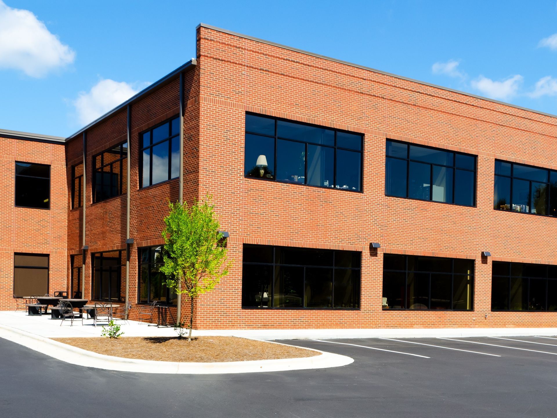 Modern two-story brick office building with large dark windows and a small tree in front