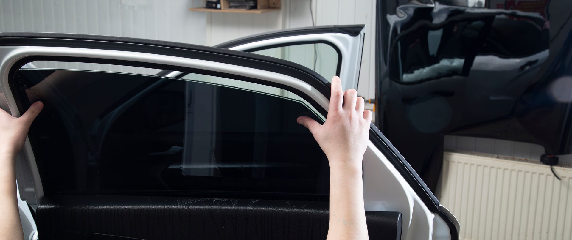 Hands holding up a car door window frame, showing a black vehicle interior.