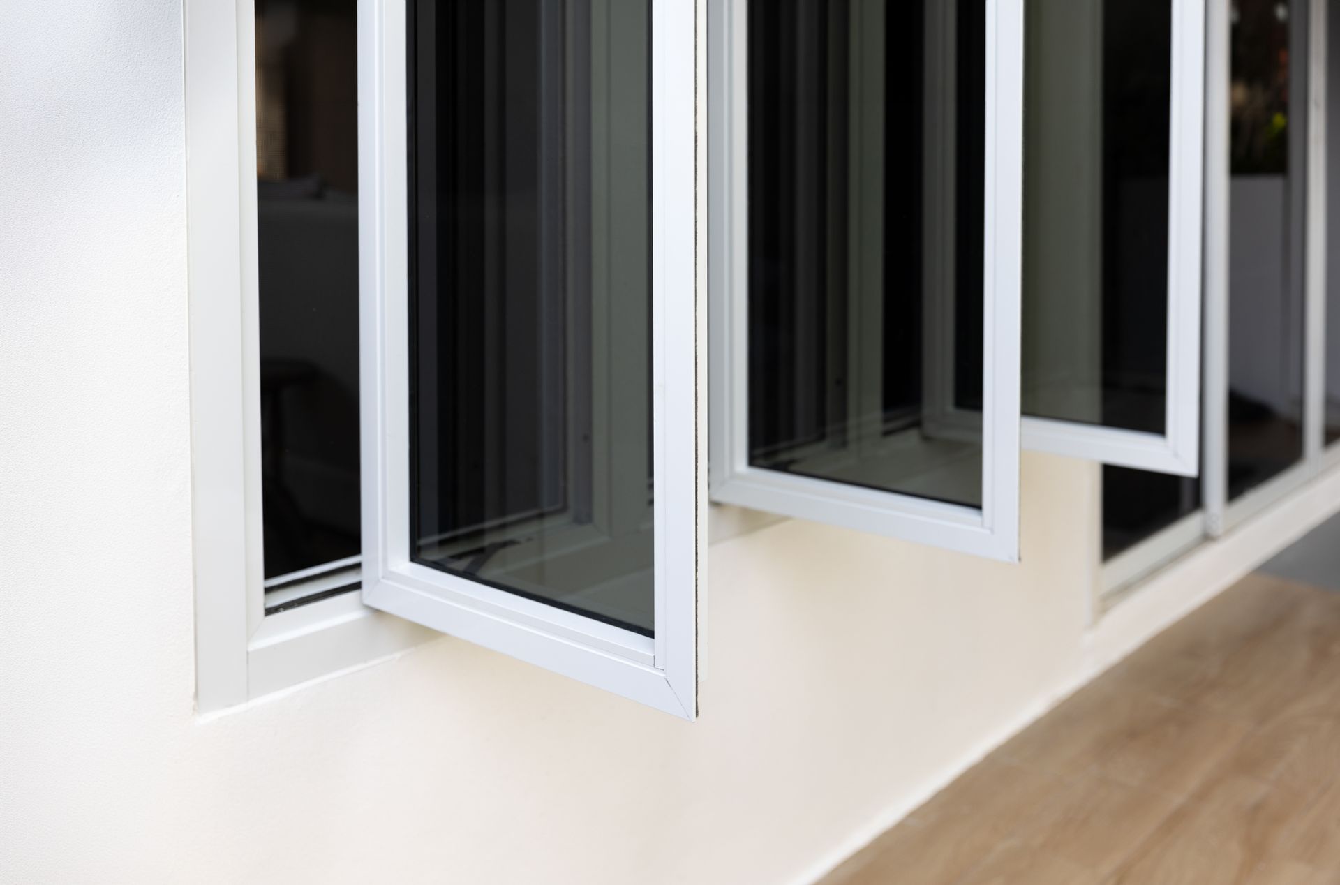 White-framed open windows along a cream wall in a bright room, with a wood floor.