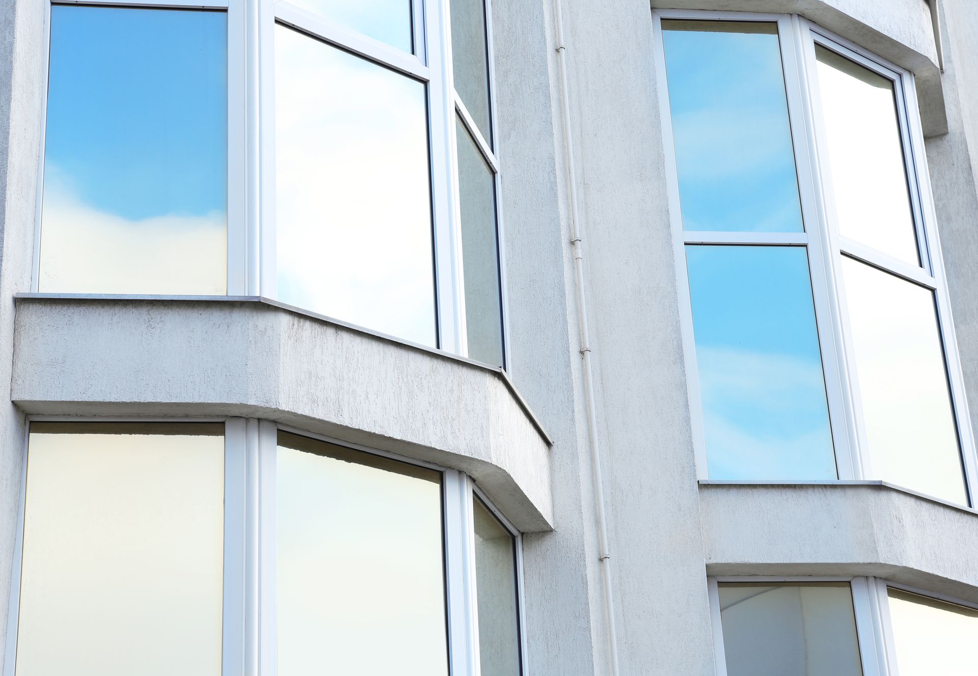Modern building facade with white-framed windows and a curved gray exterior wall against a blue sky