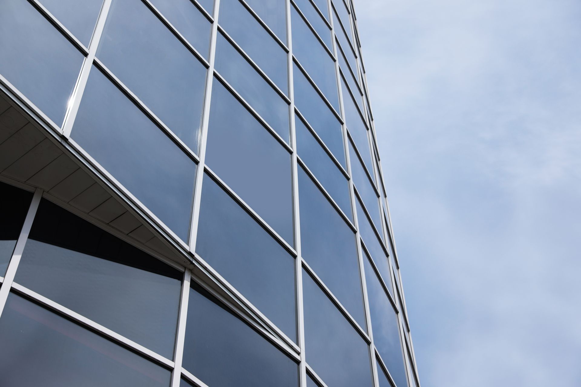 Glass office building facade viewed from below against a blue sky