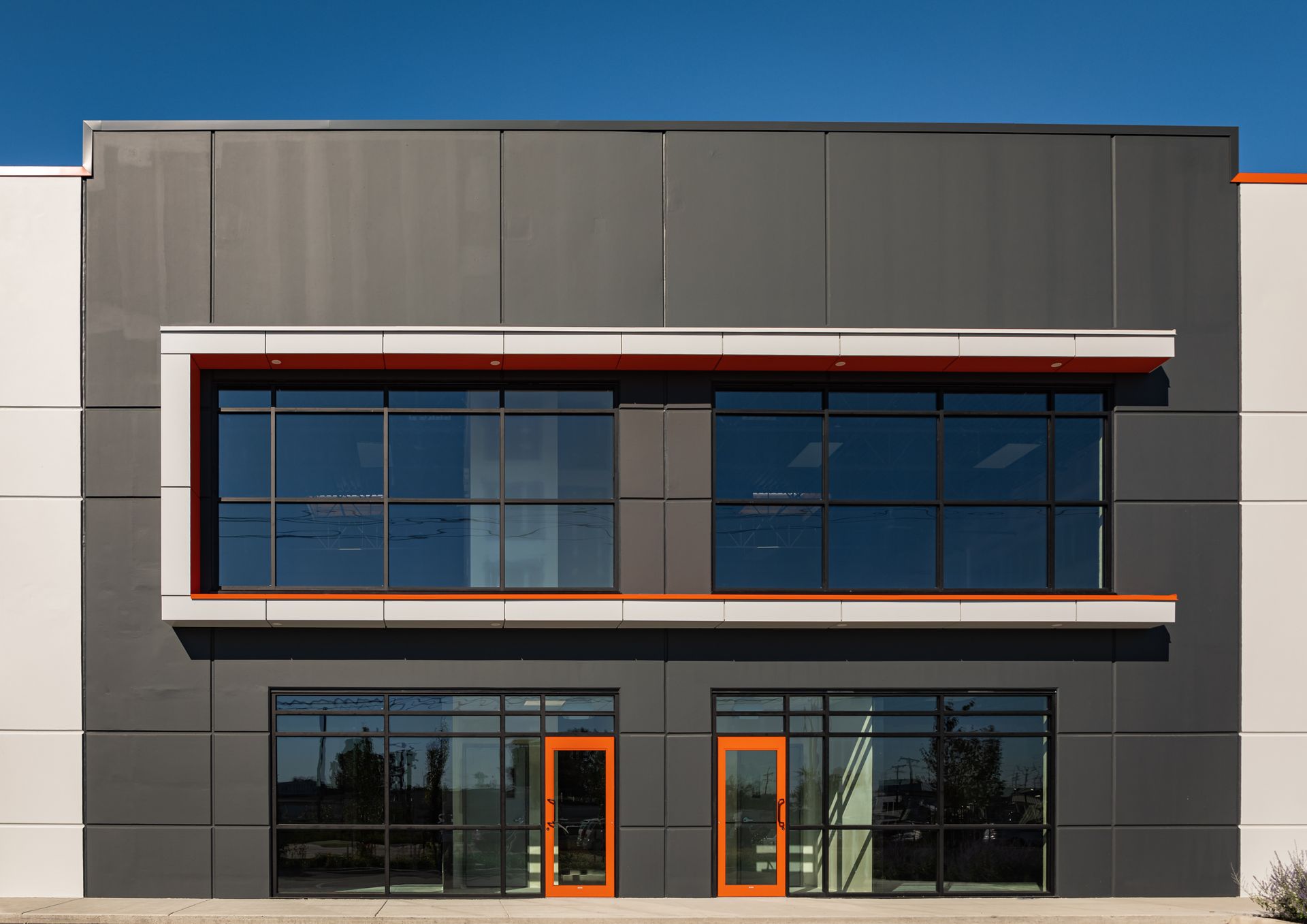 Modern gray-and-white commercial building facade with large blue-tinted windows and orange door frames