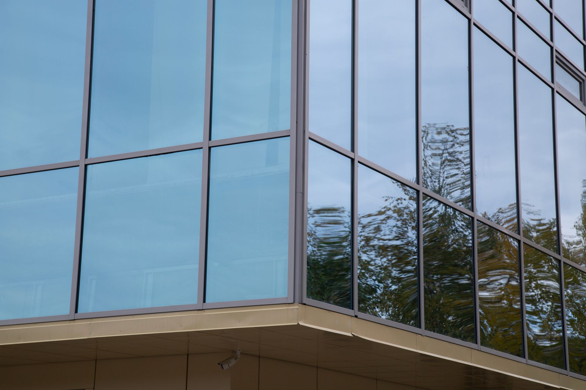 Reflective glass corner of a modern office building against blue sky and trees