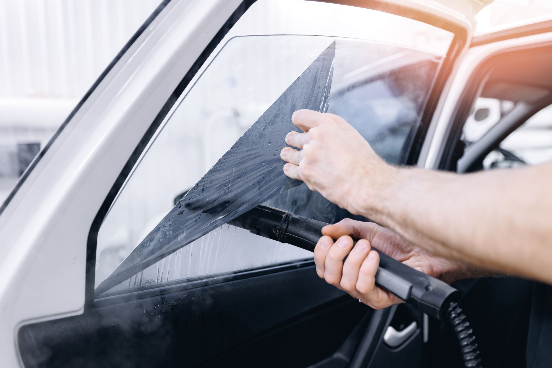 Person cleaning a car window with a squeegee and spray hose
