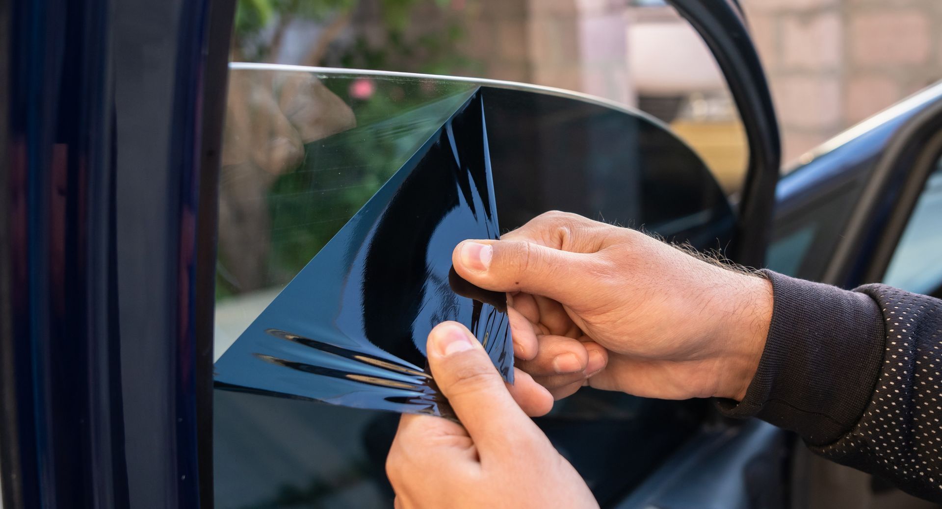 Hands removing dark window tint film from a car side window