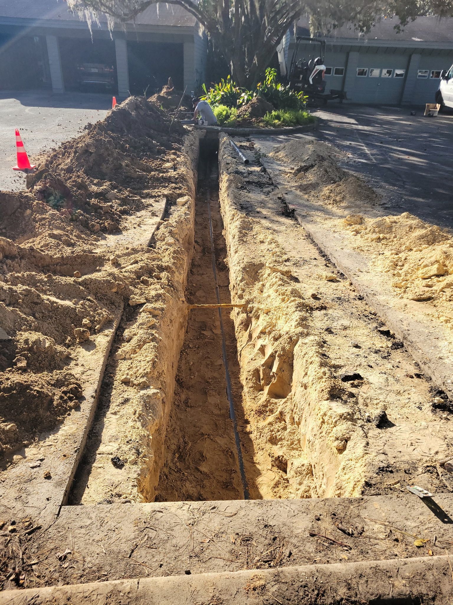 Backyard trench excavation beside a house, with piles of dirt and exposed soil in bright sunlight