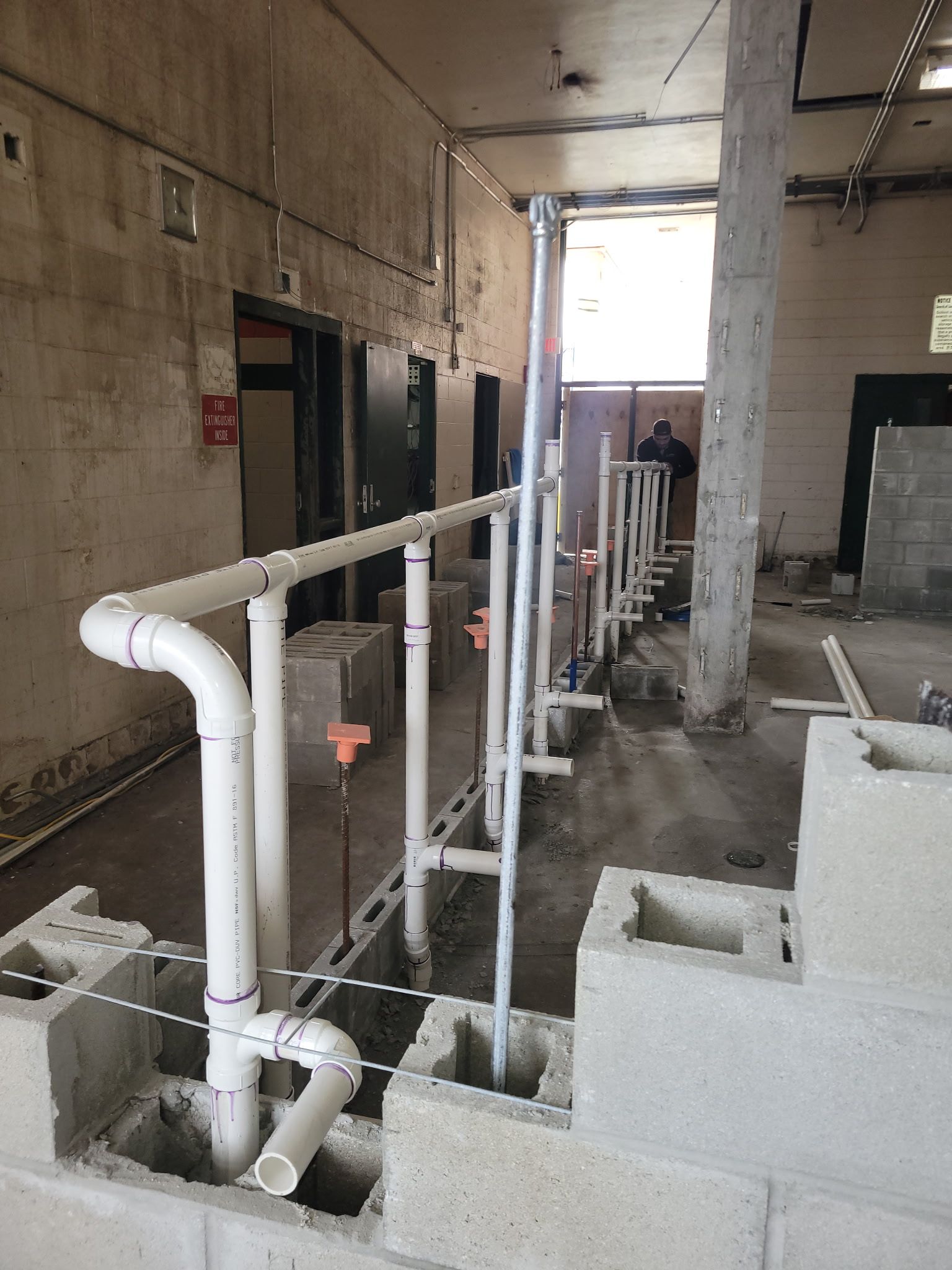 Construction worker in orange vest installing plumbing pipes in a trench at a building site.