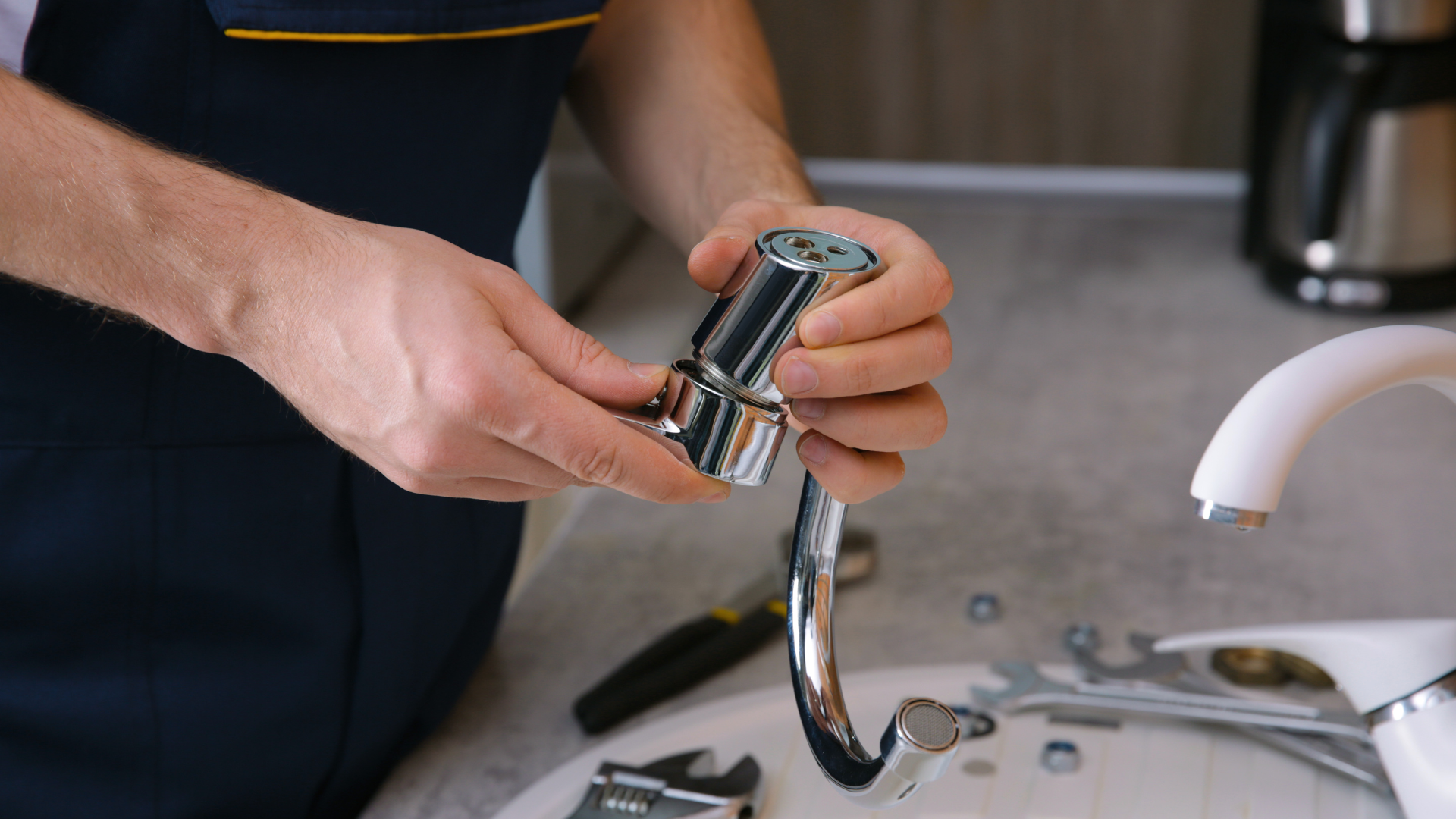 Hands holding a chrome faucet spout over a sink, with tools nearby.