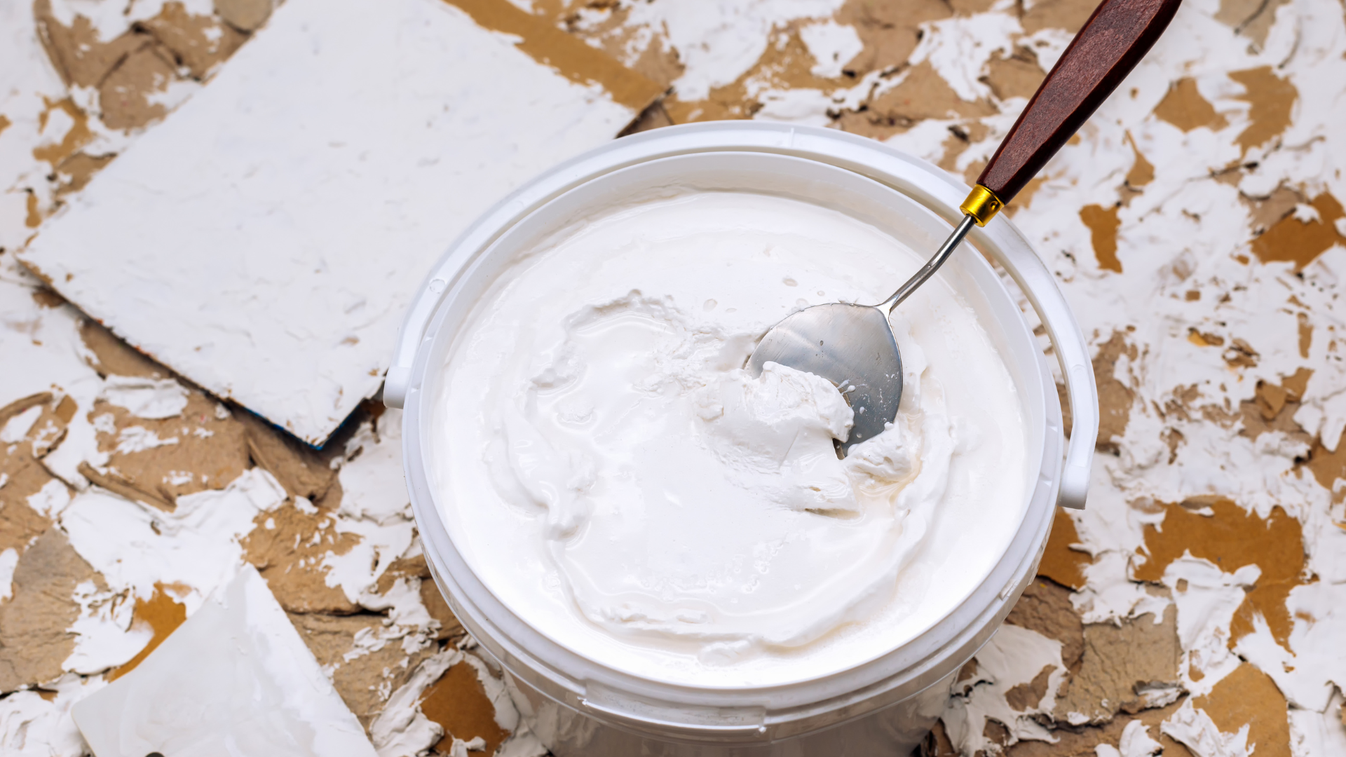 Open paint can with white paint and brush on a splattered drop cloth