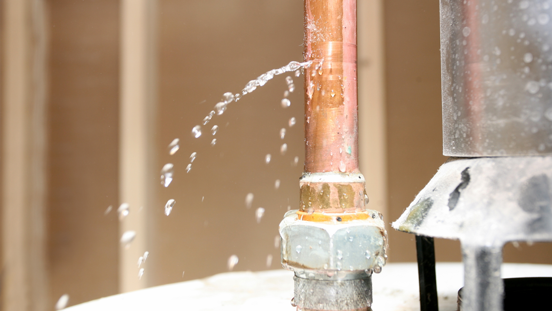 Copper pipe spraying water beside metal plumbing fixtures indoors