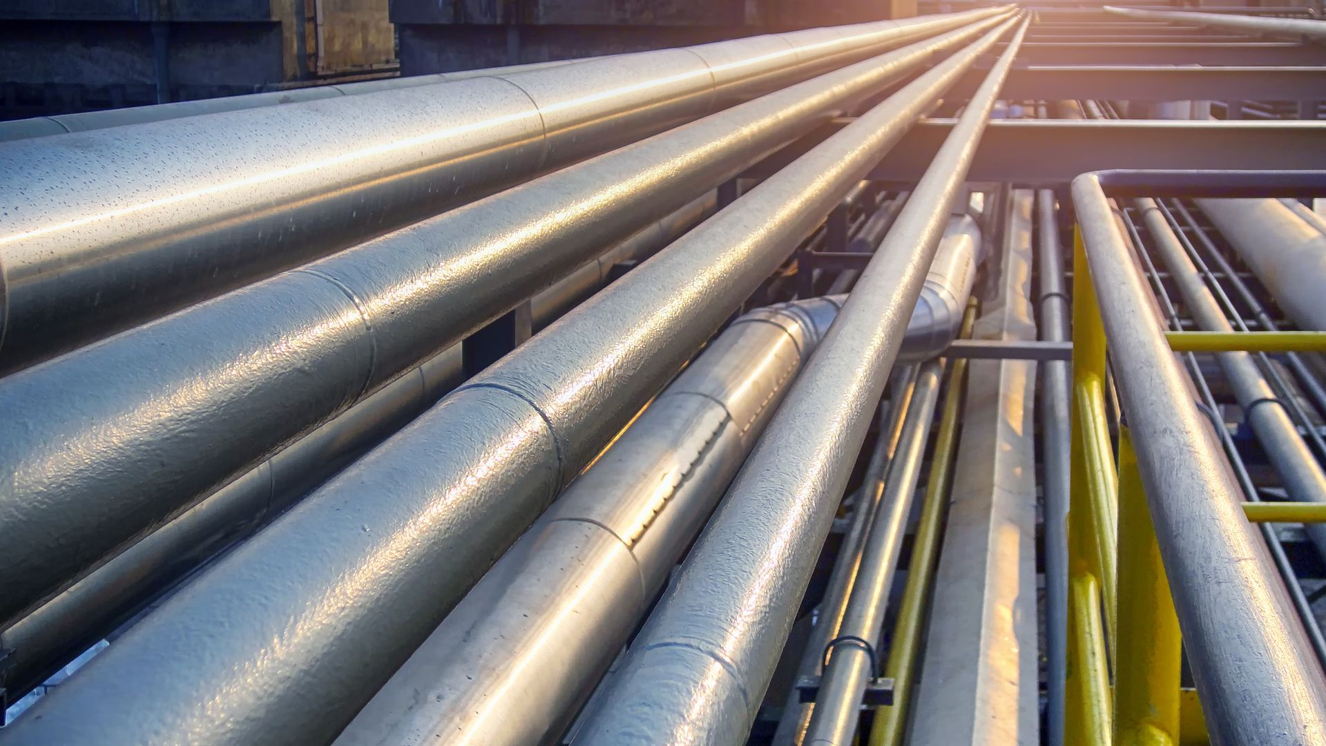 Industrial pipes in a factory silhouetted against a sunset sky.
