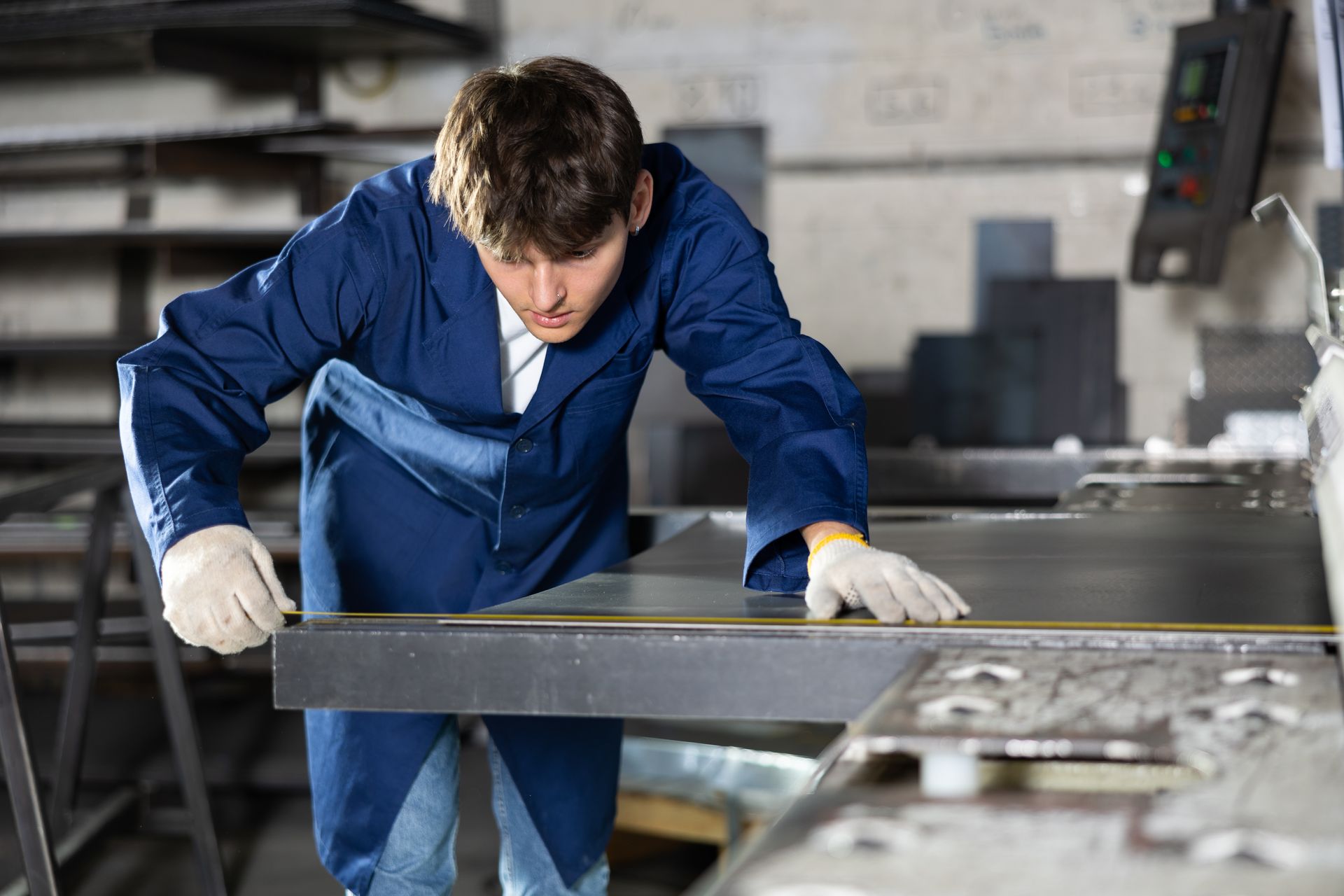A man in blue overalls is focused on working with a metal surface in a workshop setting.