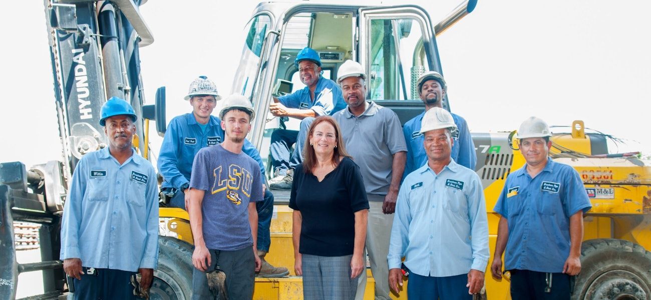 A group of construction workers are posing for a picture in front of a forklift.