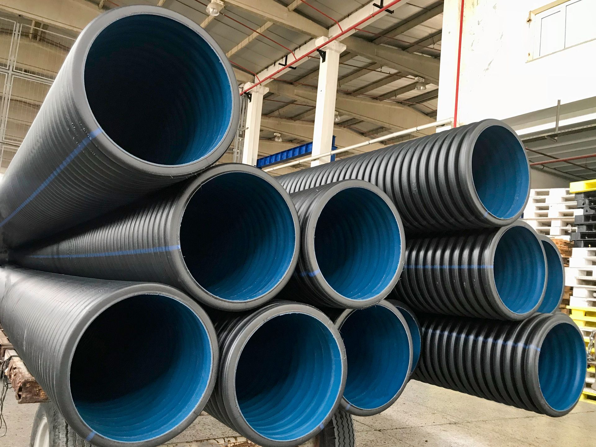 Stacked black corrugated pipes with blue interior in factory warehouse for drainage systems.