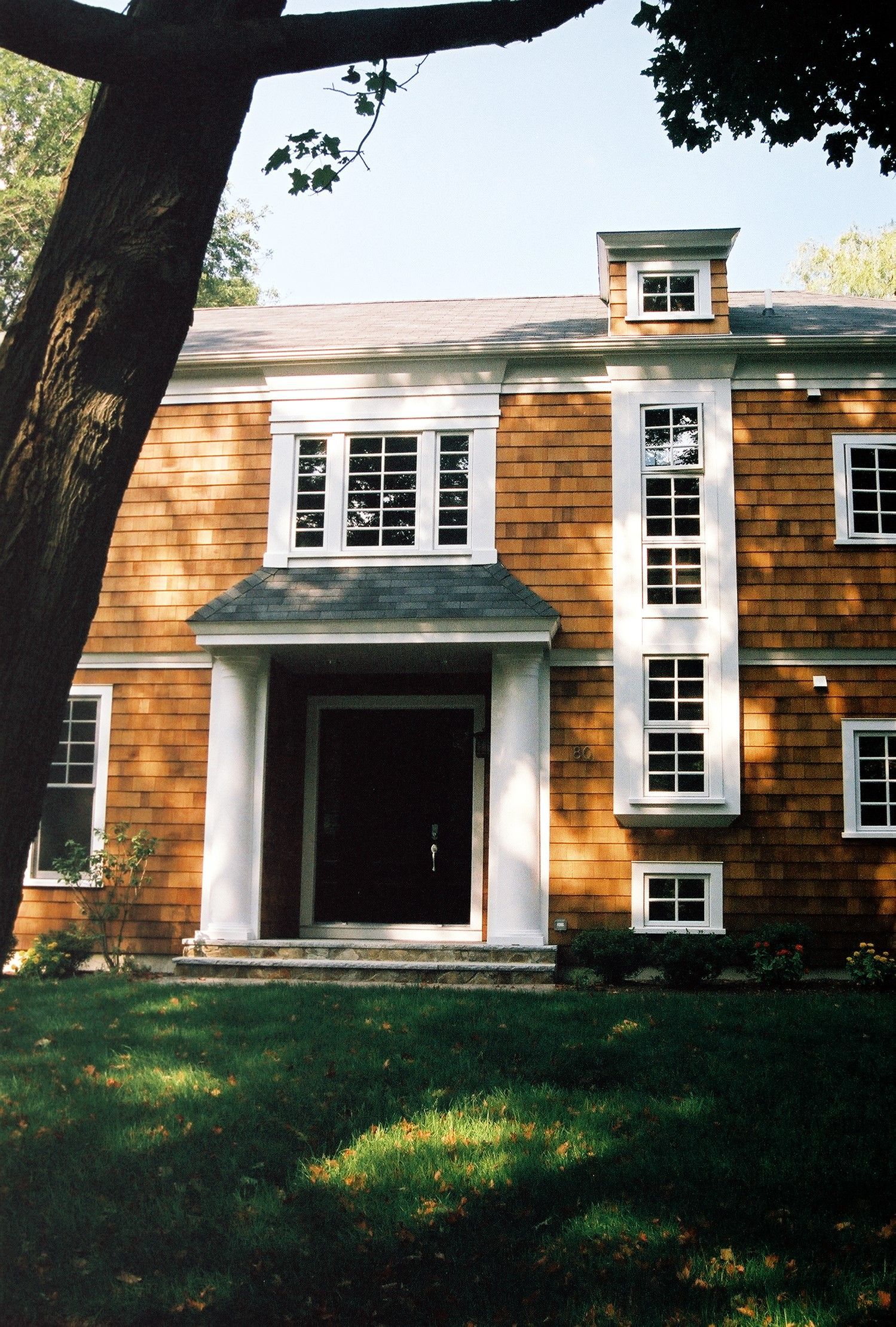 Brown two-story house with white trim. A tree in the foreground shades green grass.