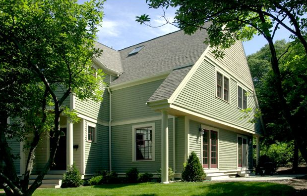 Light green house with a gabled roof, surrounded by trees.