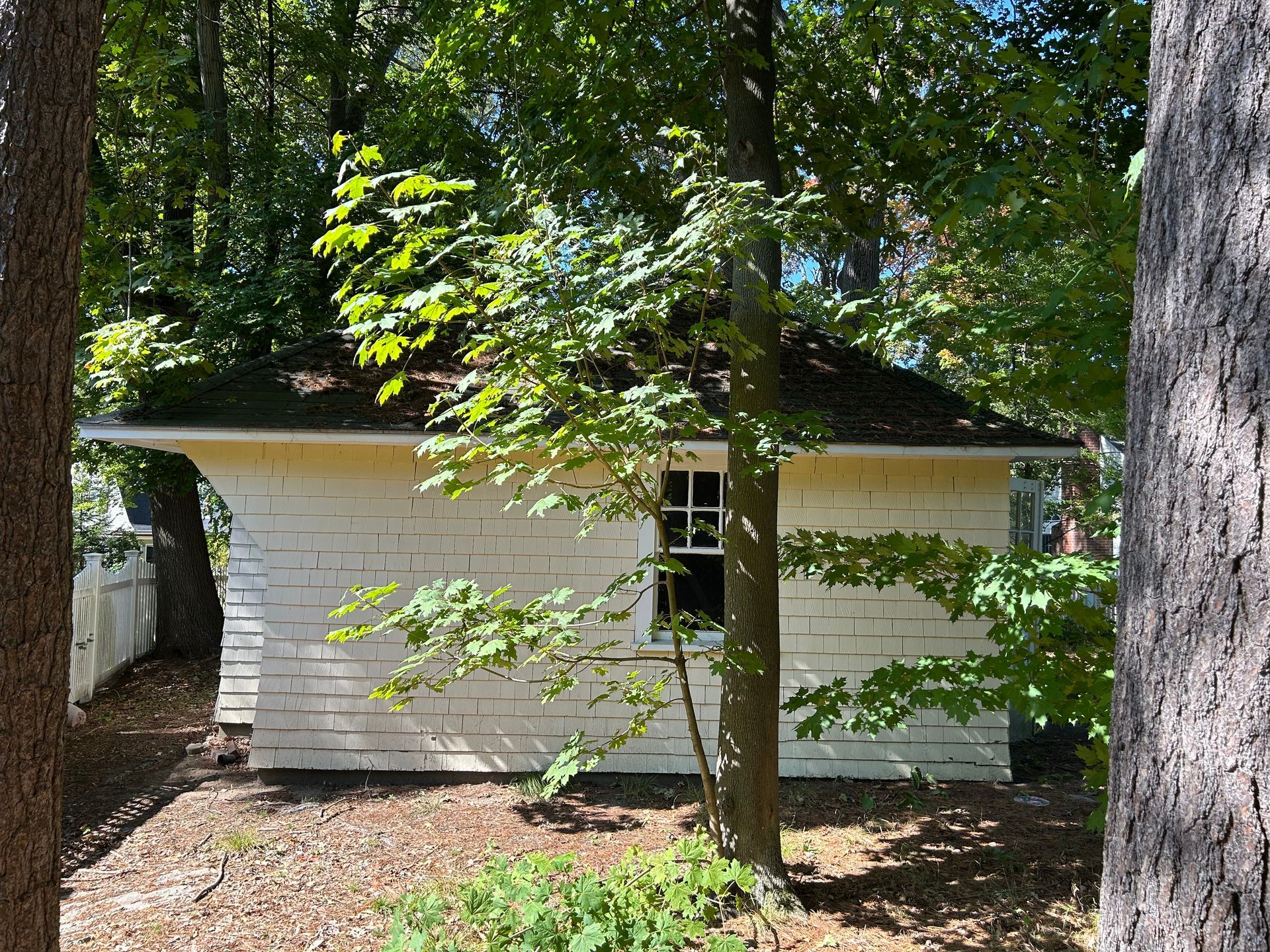 White brick building with dark roof, surrounded by trees.