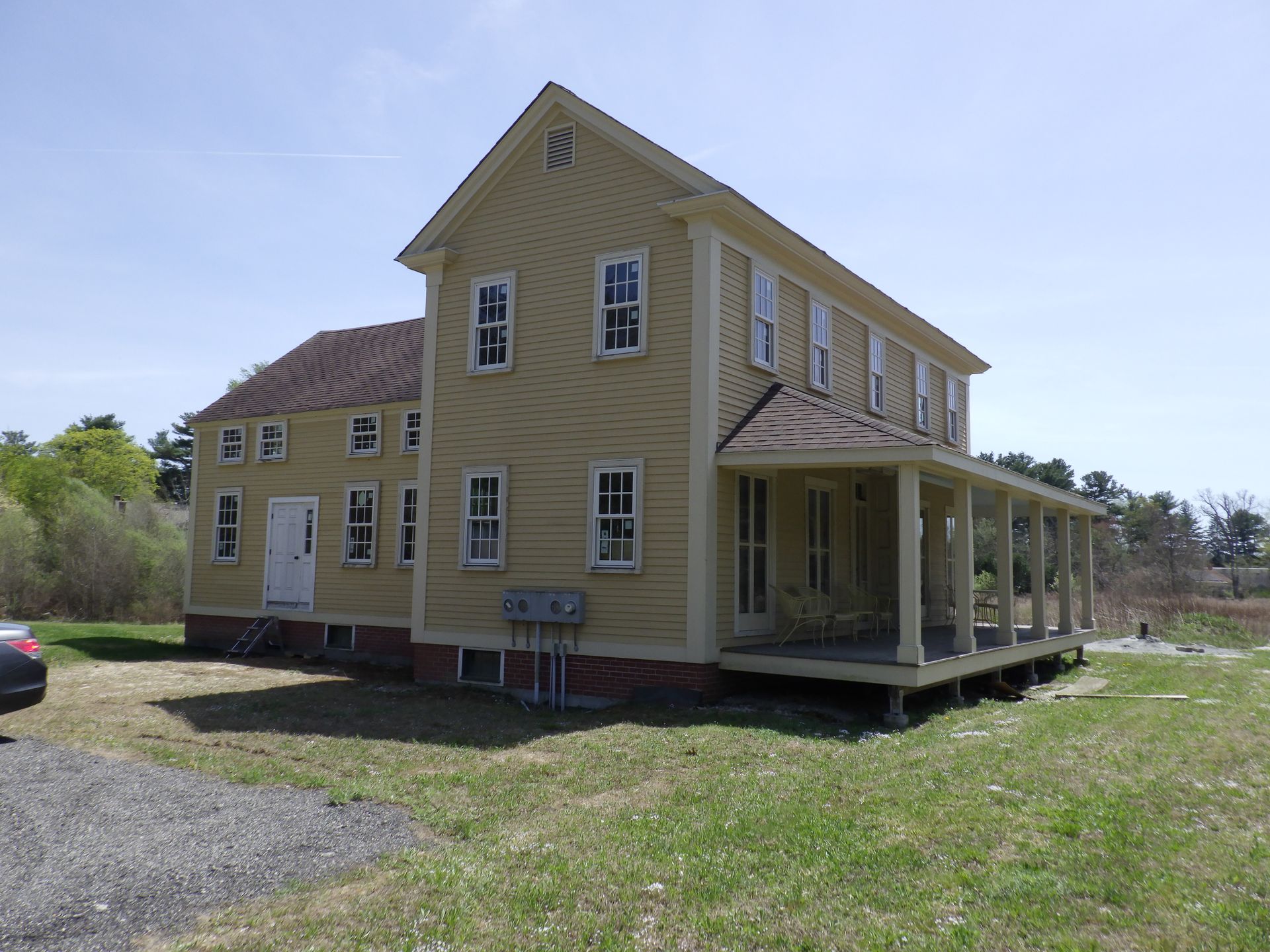 Yellow two-story house with a porch on a grassy field under a blue sky.