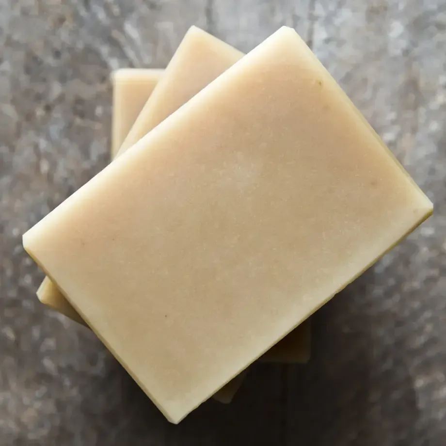 A stack of three rectangular, light beige bars of soap against a rustic wood-grain background.