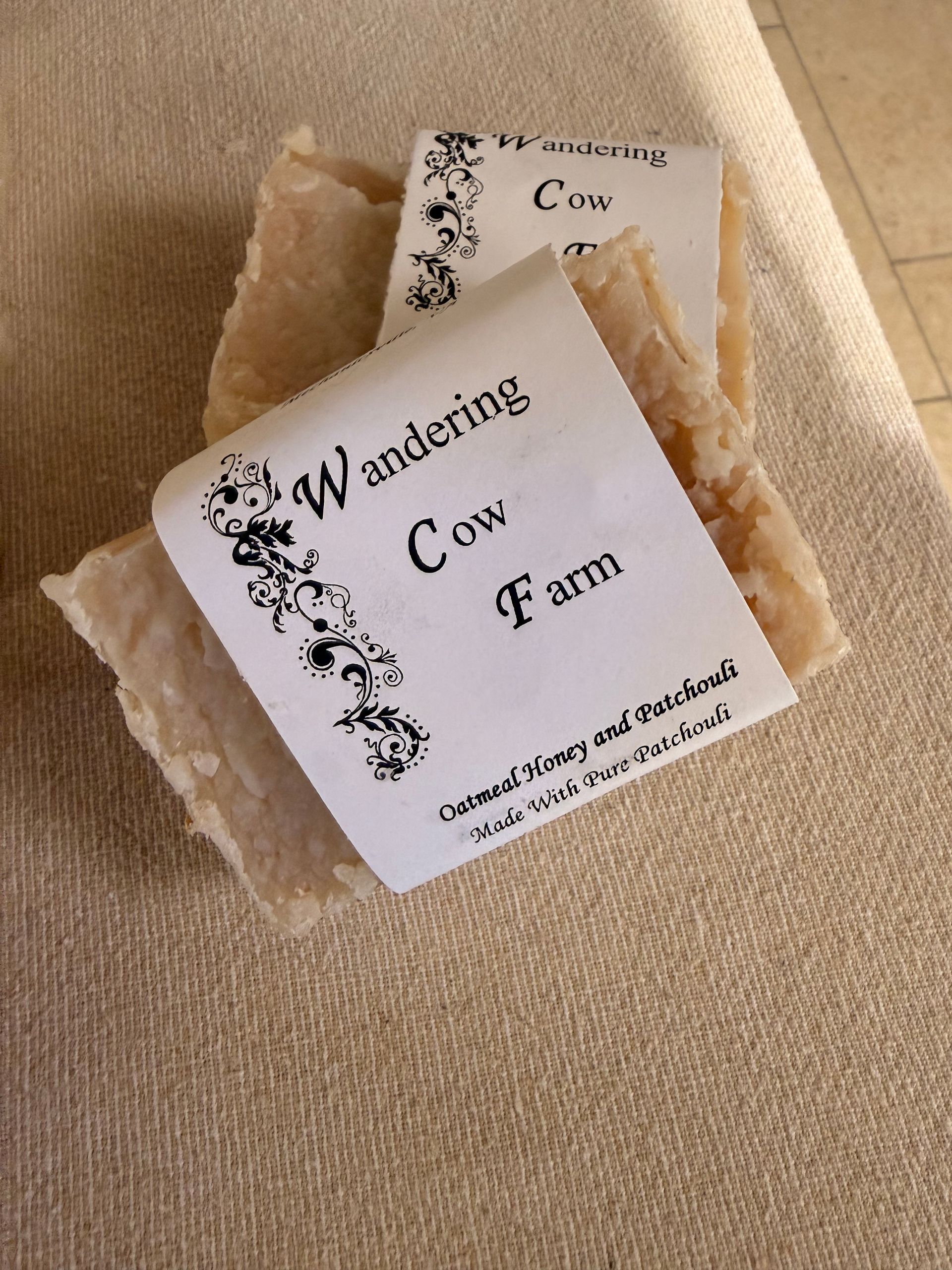 Two handmade soap bars with white labels reading “Wandering Cow Farm” on beige fabric.