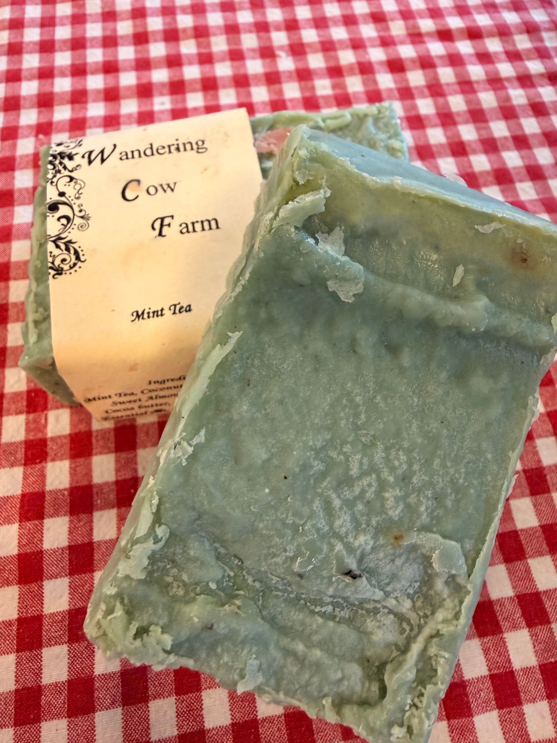 A blue-green soap bar beside a Wanderling Cow Farm label on a red-and-white checkered cloth