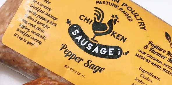 A close-up of a yellow label on a package of Pepper Sage chicken sausage, featuring a rooster logo and product text.