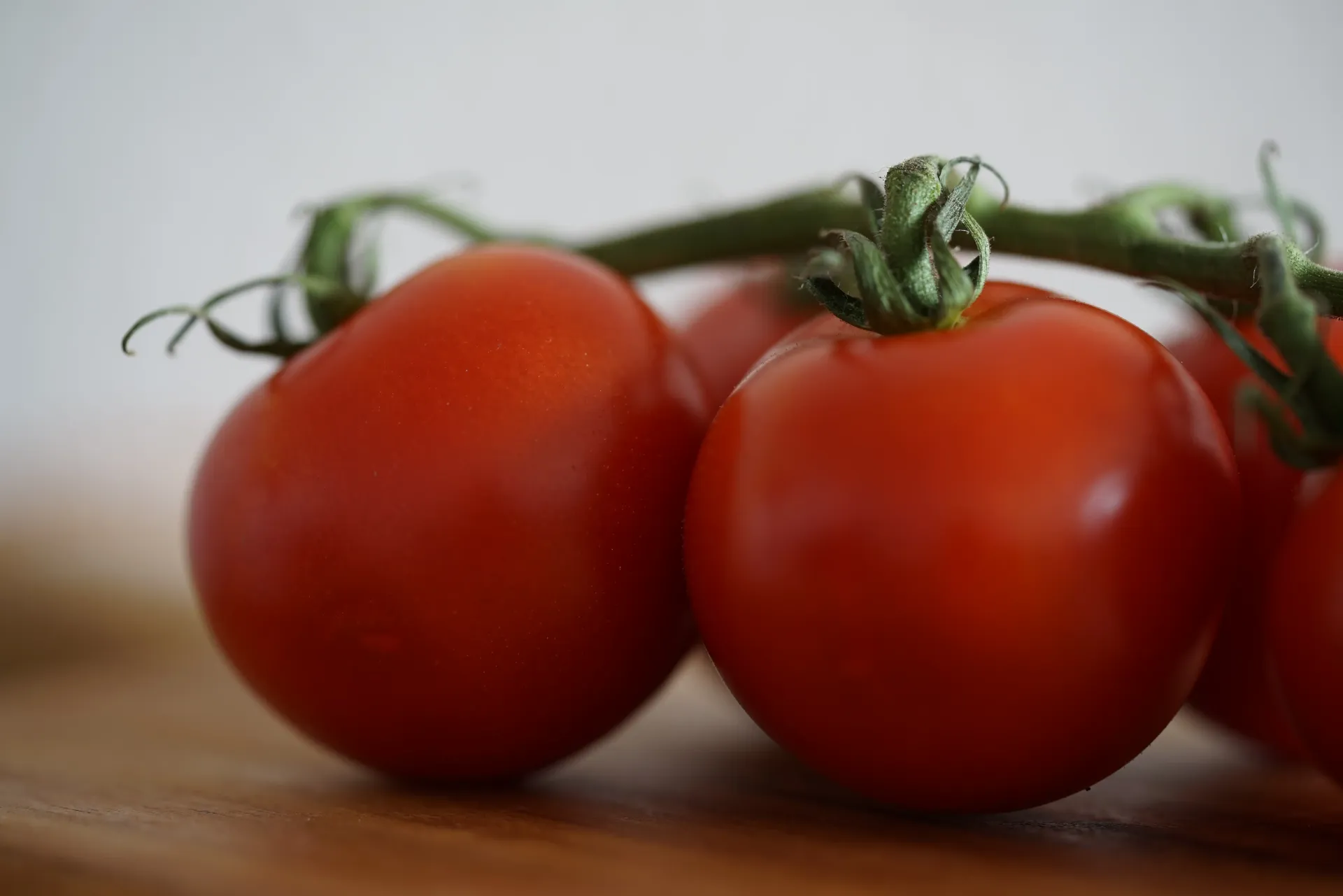 A close-up of a small cluster of bright red tomatoes still attached to their green vine on a wooden surface.