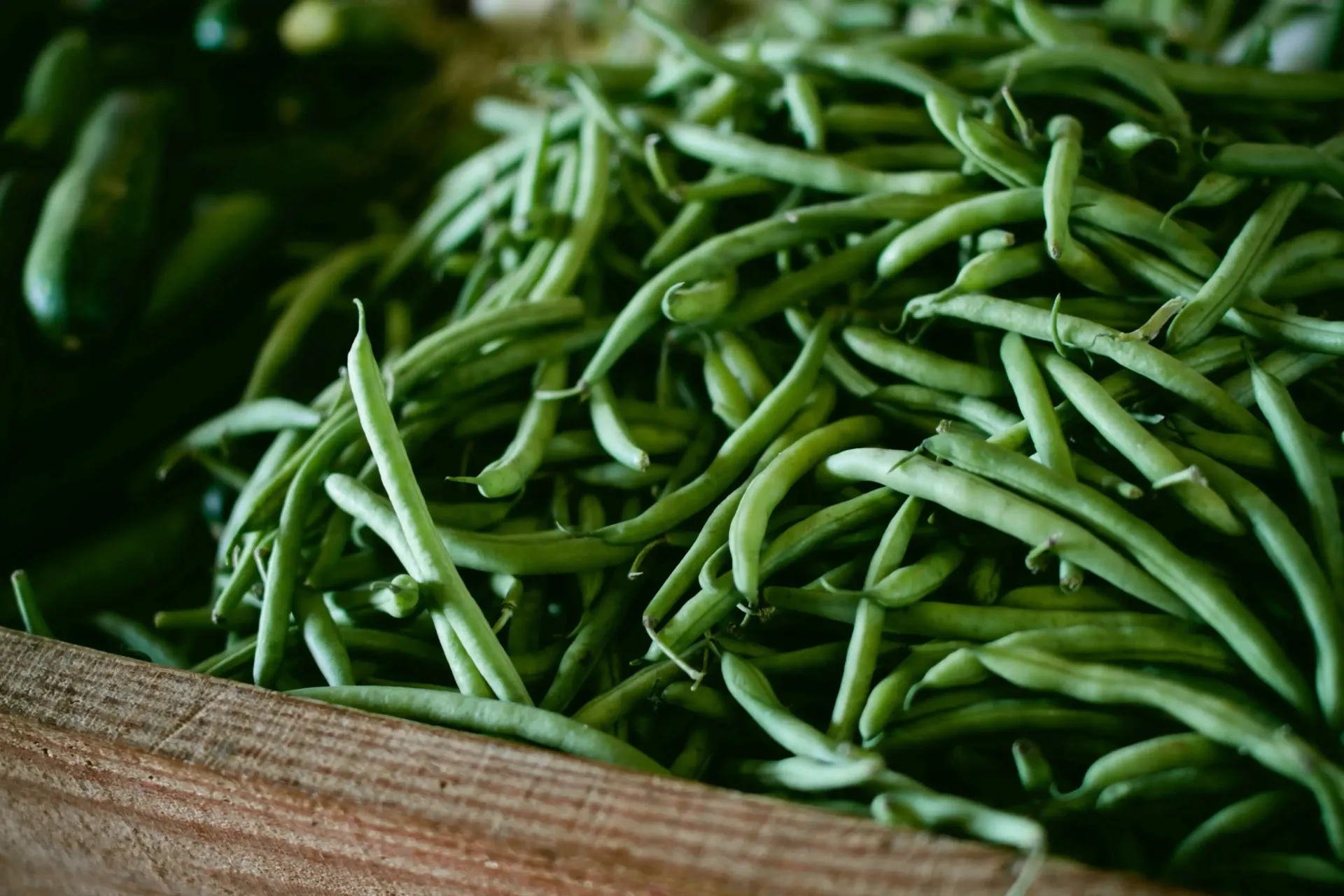 A wooden crate filled with fresh, vibrant green beans at a market.