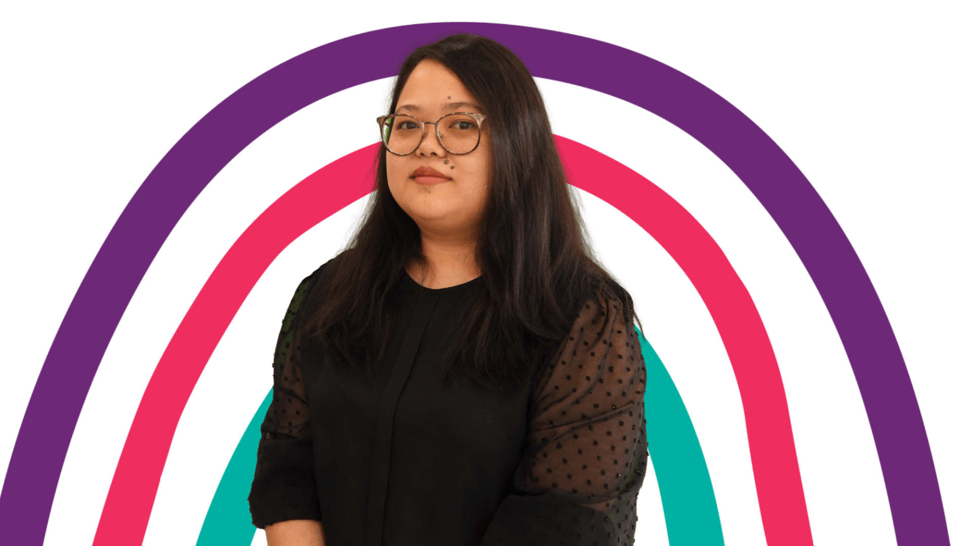 A woman wearing glasses is standing in front of a rainbow.