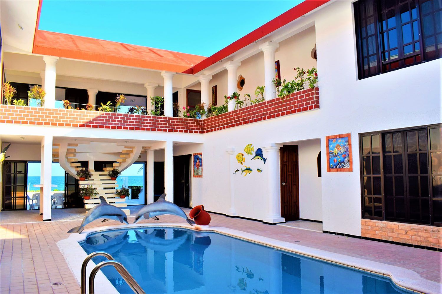 Pool in courtyard of a white building with red roof, ocean view and dolphin statues.