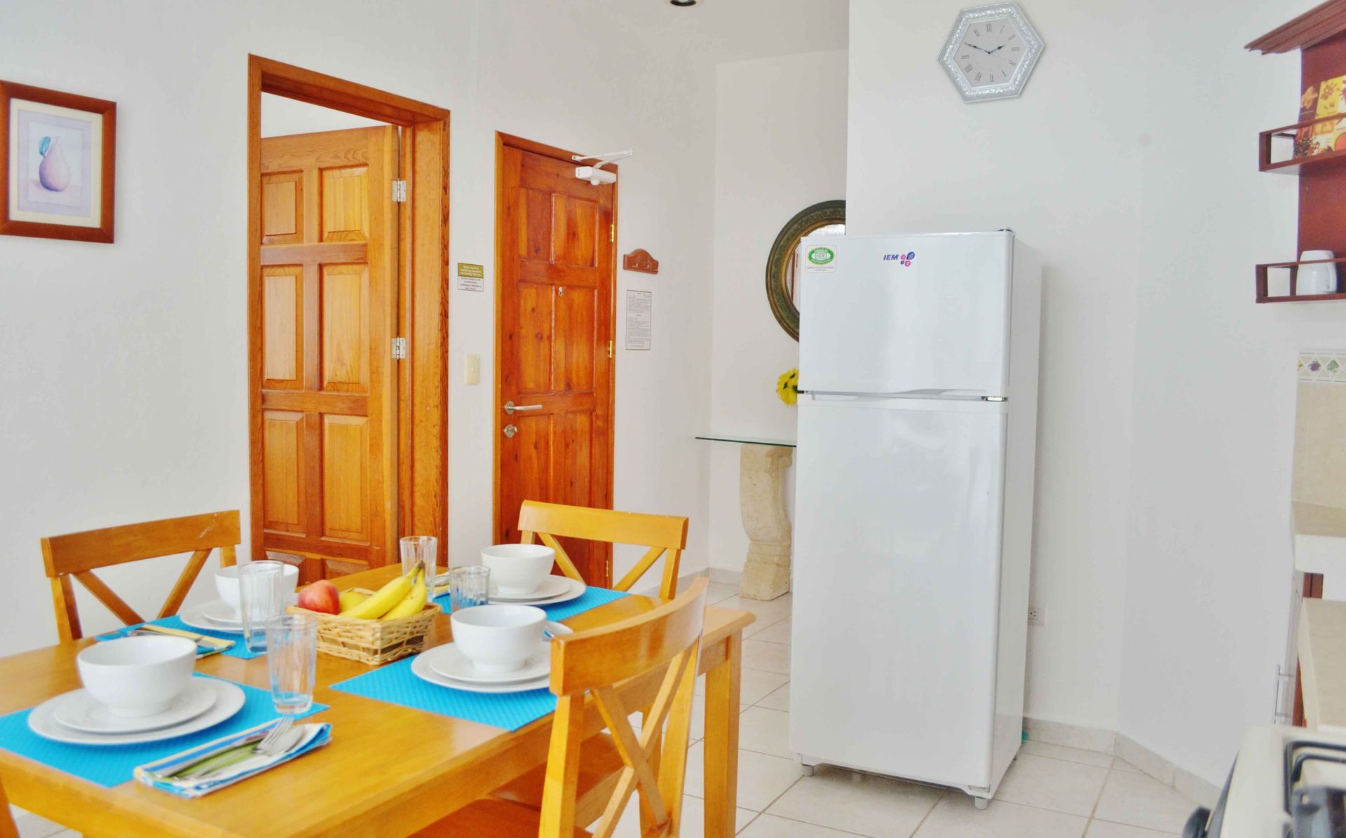 Comedor con mesa y sillas de madera, y un refrigerador blanco. Se ven dos puertas.
