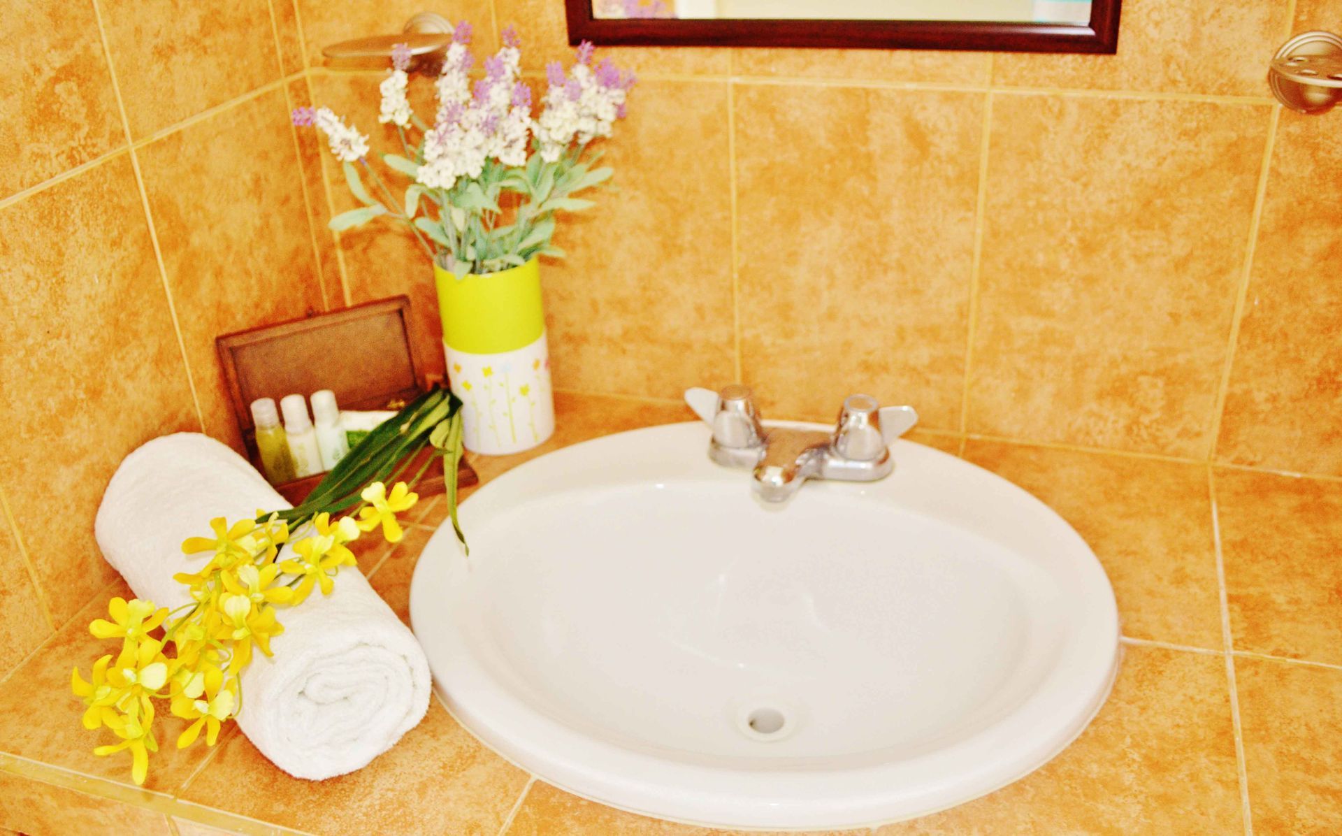 White sink in bathroom with floral decorations and rolled towel on tiled wall.
