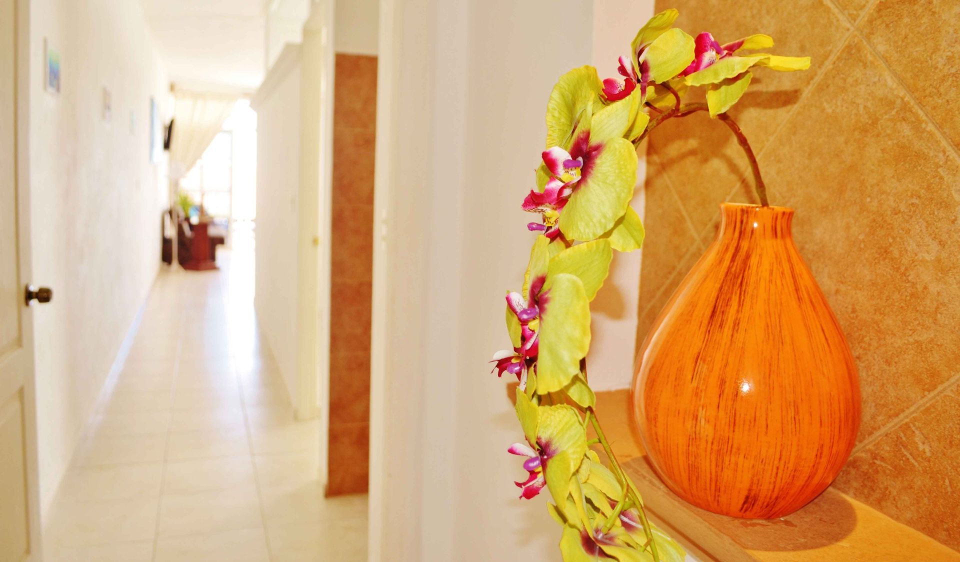 Orange vase with flower stems, on ledge near a hallway.