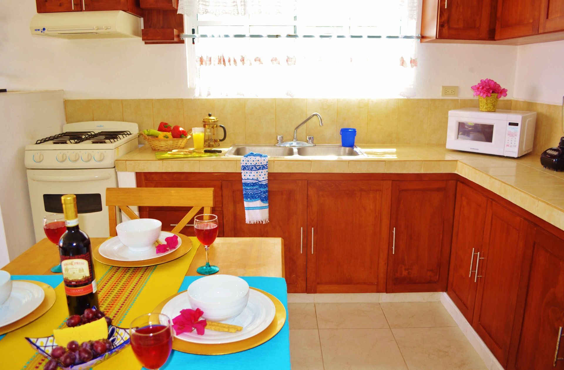 Cocina con armarios de madera, fogones, microondas y mesa puesta con vajilla y copas de vino.