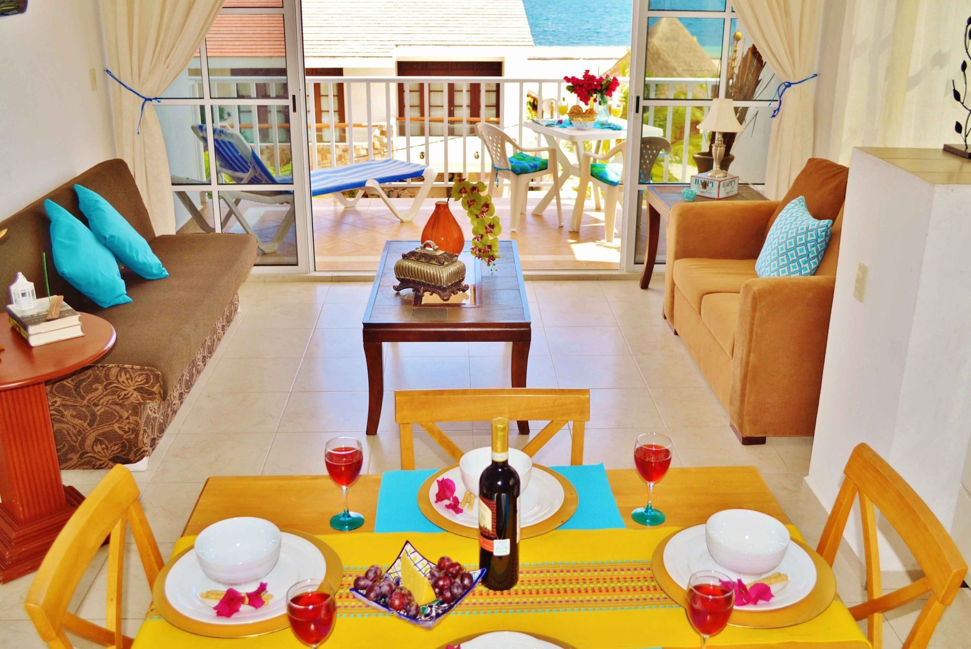 Salón con vistas al balcón, sofá marrón, mesa de comedor amarilla para dos personas, detalles turquesa.